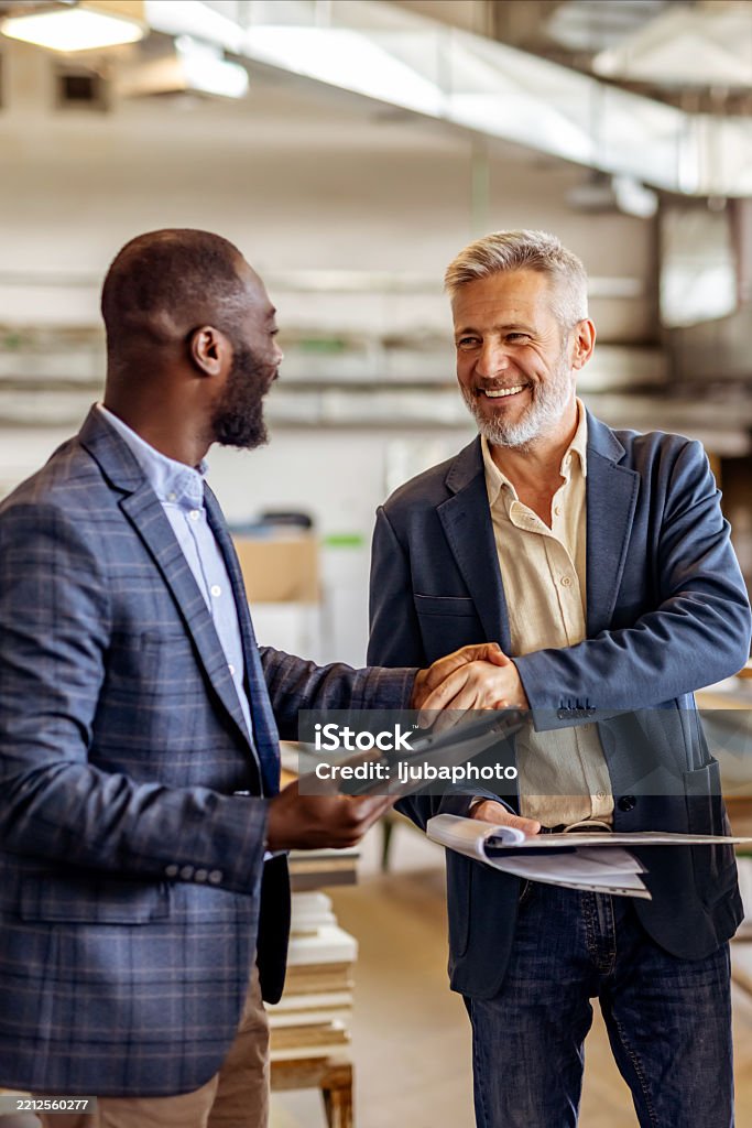 Two professionals in jackets sharing a handshake in a modern office, symbolizing business collaboration, partnership, and professional success. Their engagement conveys a sense of teamwork, making agreements, and friendly connection.