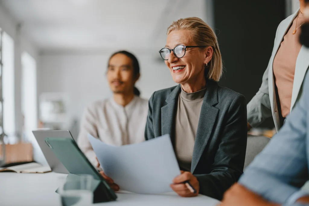 Confident senior businesswoman leading a team during an office meeting, showcasing collaboration and leadership in a professional workplace environment.
